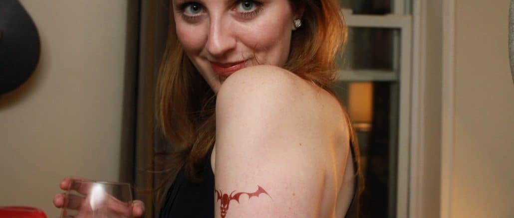 A woman holding a glass of wine with a tatoo on her shoulder