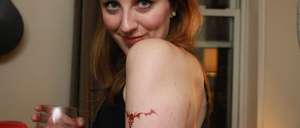 A woman holding a glass of wine with a tatoo on her shoulder