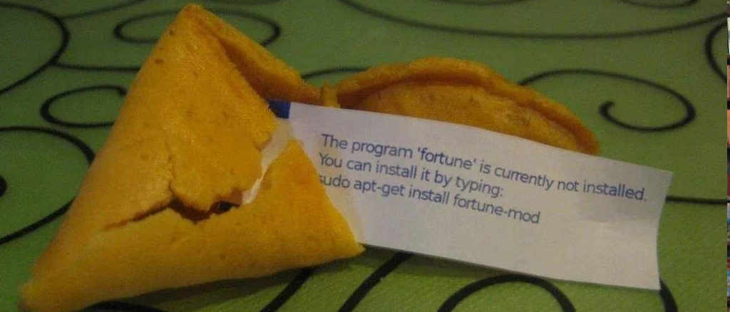 A fortune cookie disgorging a scrap of paper onto a green tablecloth