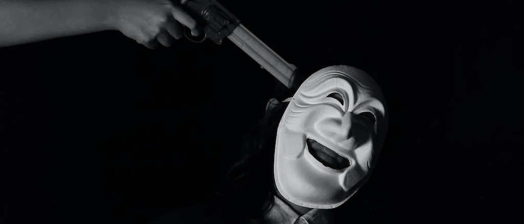 Black and white photo of a masked man  with a gun to his head