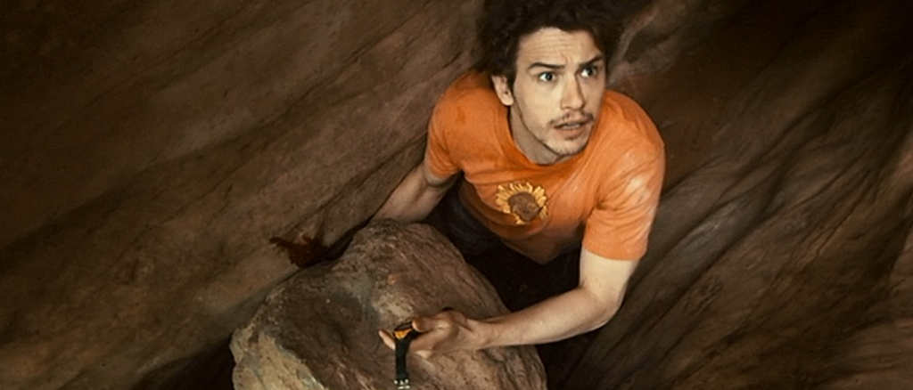 A man holding a watch with his arm trapped behind a rock