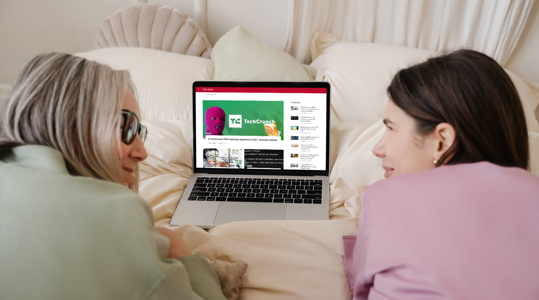 Two women looking at each other over a laptop on a bed