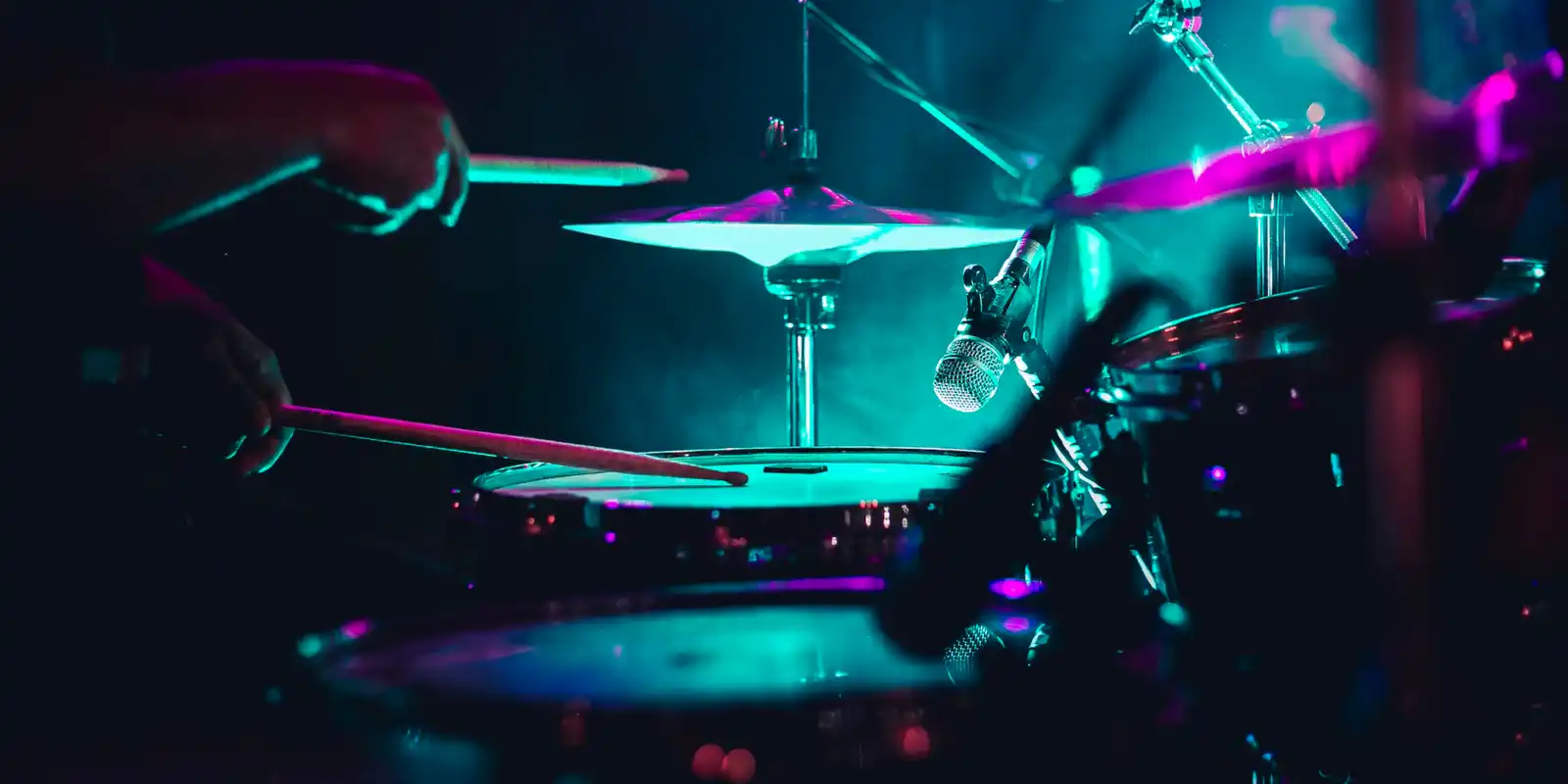 drummer drumming at a concert with turquoise and purple lights