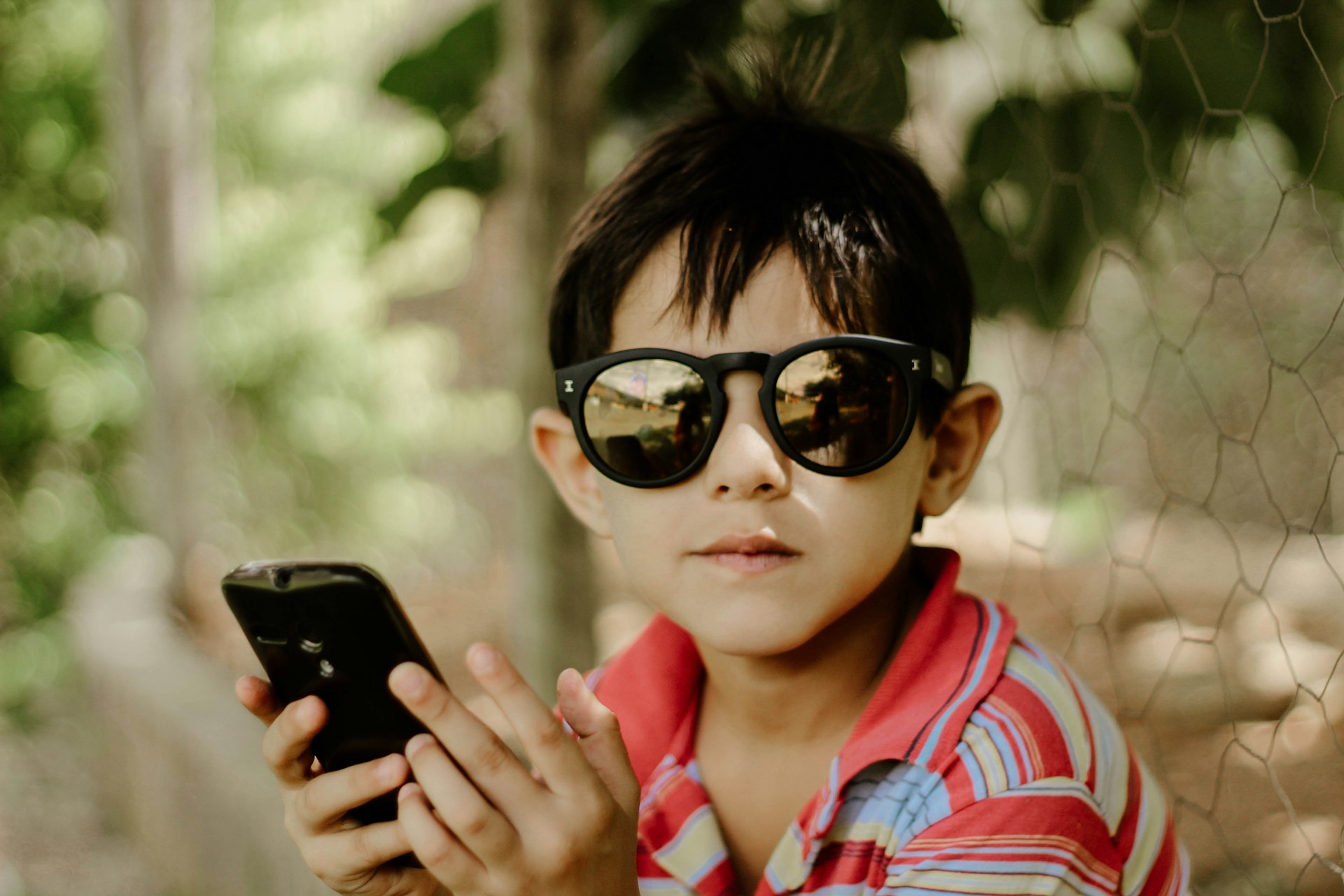 A boy wearing sunglasses and holding a phone
